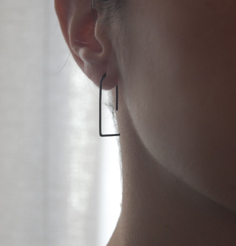 May include: A pair of black minimalist hoop earrings. The earrings are made of thin metal and have a simple, geometric design.