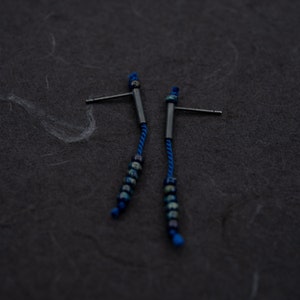 Pair of 38 mm length pendant earrings handmade in black sterling silver tube with a blue silk cord threaded through the center for hanging Miyuki beads in Picasso cobalt blue. Designed and crafted by hand in Paris by A g J c