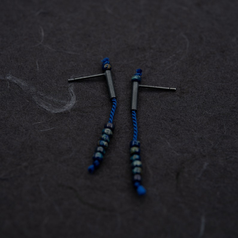 Pair of 38 mm length pendant earrings handmade in black sterling silver tube with a blue silk cord threaded through the center for hanging Miyuki beads in Picasso cobalt blue. Designed and crafted by hand in Paris by A g J c