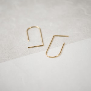May include: A pair of gold-toned, minimalist earrings with a simple, curved design. The earrings are made of thin metal and have a delicate, modern aesthetic.