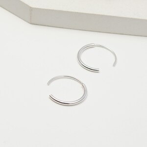May include: A pair of silver hoop earrings. The hoops are simple and sleek, with a smooth, polished finish.
