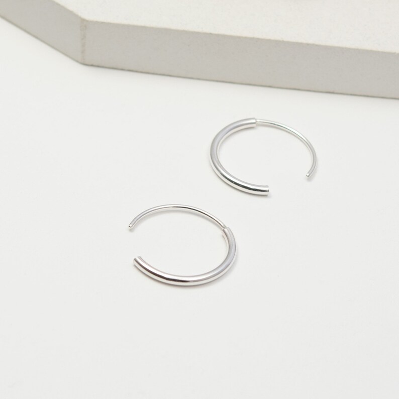 May include: A pair of silver hoop earrings. The hoops are simple and sleek, with a smooth, polished finish.