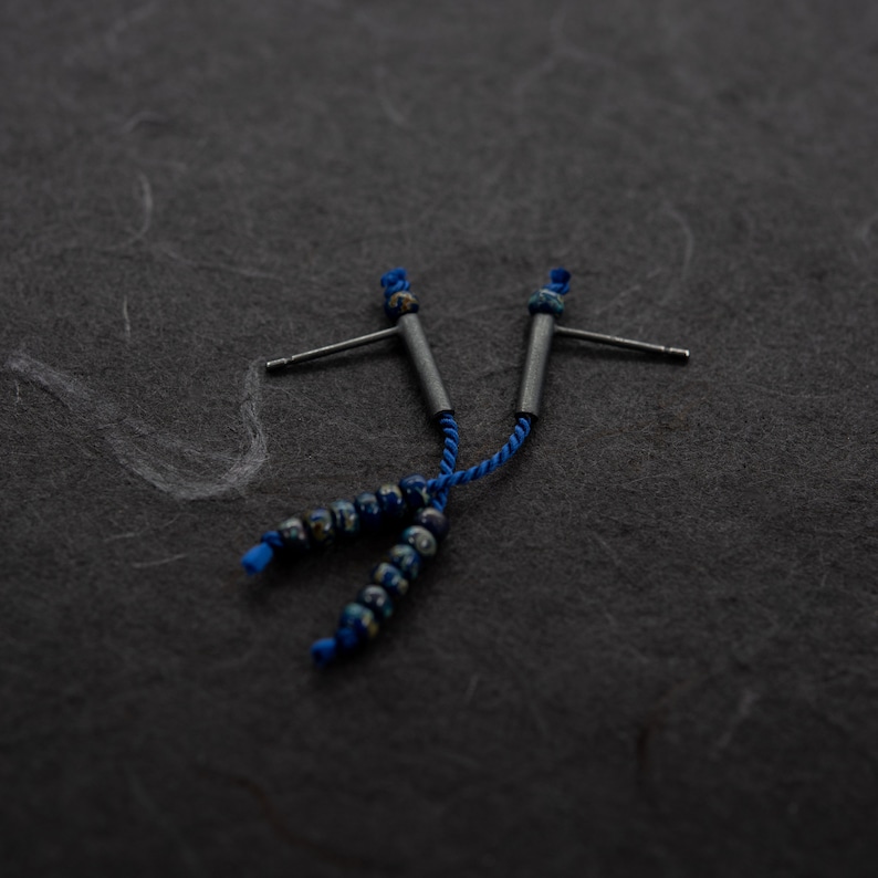 Pair of 38 mm length pendant earrings handmade in oxidized sterling silver tube with a blue silk cord threaded through the center for hanging Miyuki beads in Picasso cobalt blue. Designed and crafted by hand in Paris by A g J c
