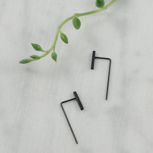 May include: A pair of black minimalist earrings with a straight bar and a thin, angled wire.