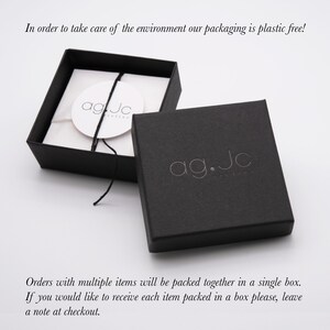 May include: A black jewelry box with the text "ag.Jc" printed on the top. The box is open and the inside is lined with white paper. The text "agJc" is printed on a white circle inside the box.