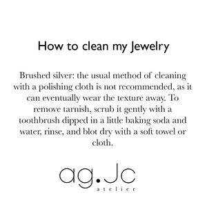 May include: Instructions on how to clean brushed silver jewelry. The text explains that polishing cloths are not recommended, and suggests using baking soda and a toothbrush to remove tarnish. The text is followed by the logo "ag.Jc atelier".