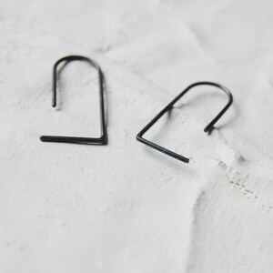 May include: Two black metal earrings with a simple, geometric design. The earrings are shaped like a rounded rectangle.