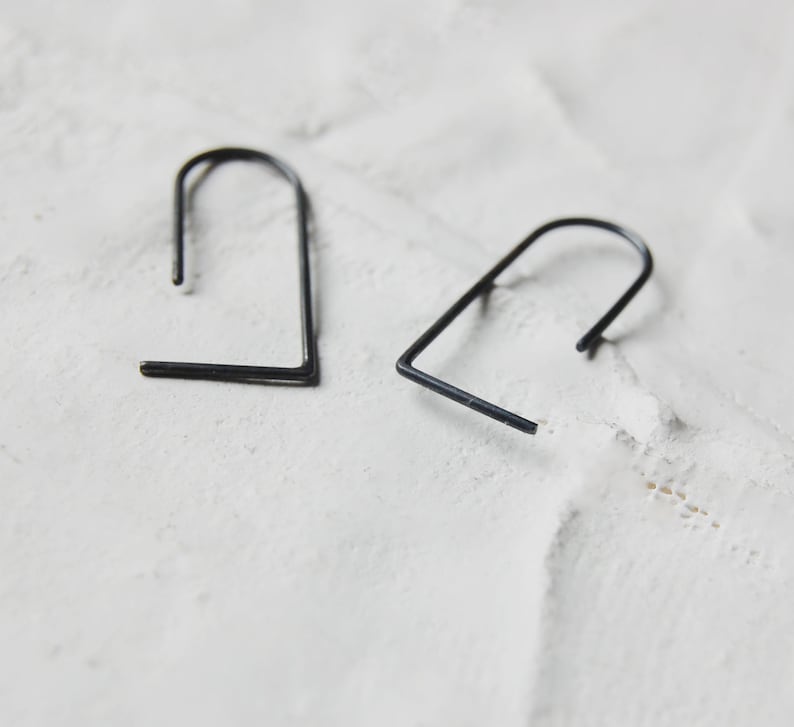 May include: Two black metal earrings with a simple, geometric design. The earrings are shaped like a rounded rectangle.