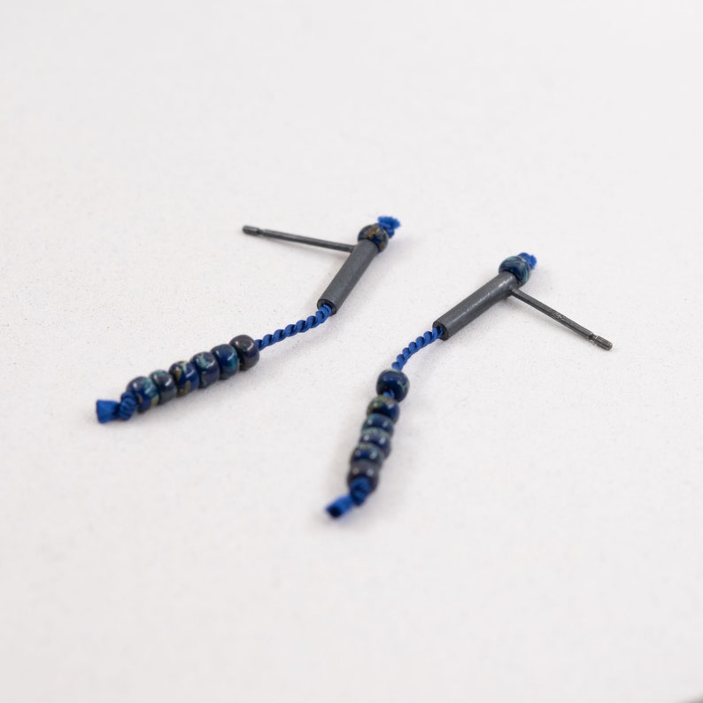 Pair of 38 mm length pendant earrings handmade in oxidized sterling silver tube with a blue silk cord threaded through the center for hanging Miyuki beads in Picasso cobalt blue. Designed and crafted by hand in Paris by A g J c