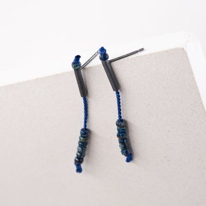 Pair of 38 mm length pendant earrings handmade in black sterling silver tube with a blue silk cord threaded through the center for hanging Miyuki beads in Picasso cobalt blue. Designed and crafted by hand in Paris by A g J c