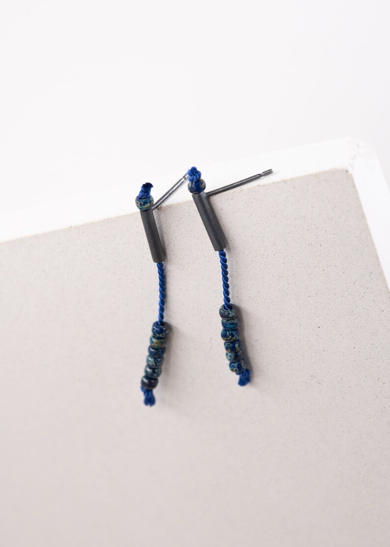 Pair of 38 mm length pendant earrings handmade in black sterling silver tube with a blue silk cord threaded through the center for hanging Miyuki beads in Picasso cobalt blue. Designed and crafted by hand in Paris by A g J c