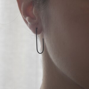 May include: A pair of black hoop earrings worn in a person's earlobe.