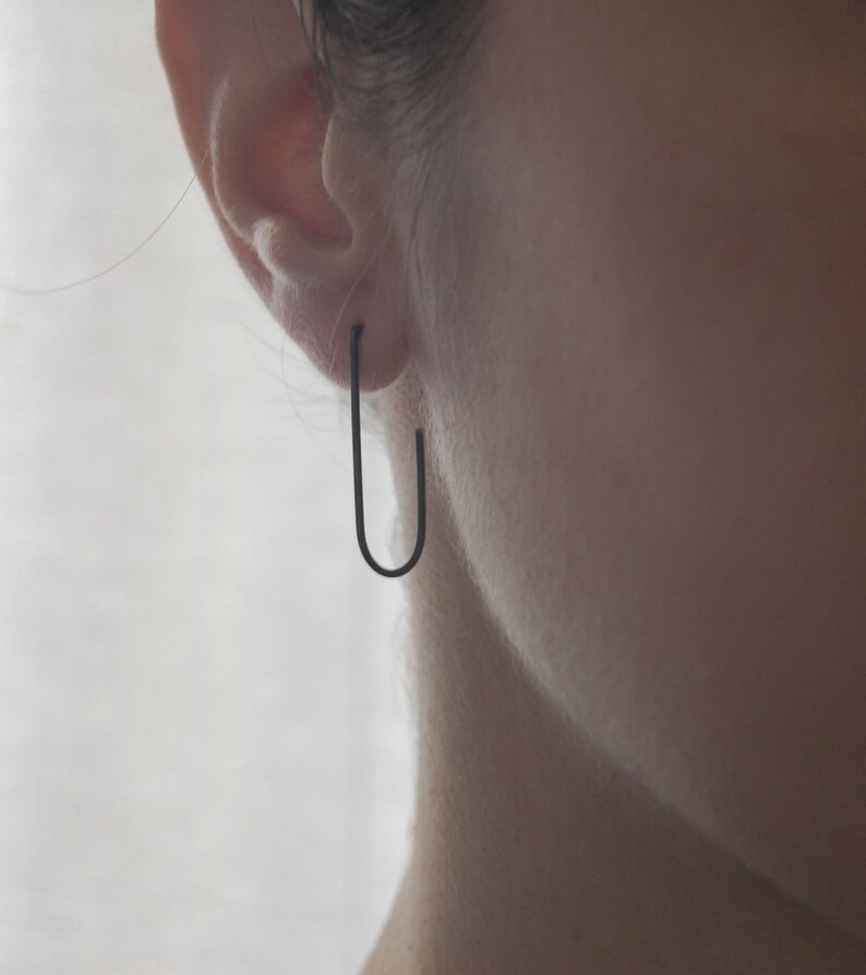 May include: A pair of black hoop earrings worn in a person's earlobe.