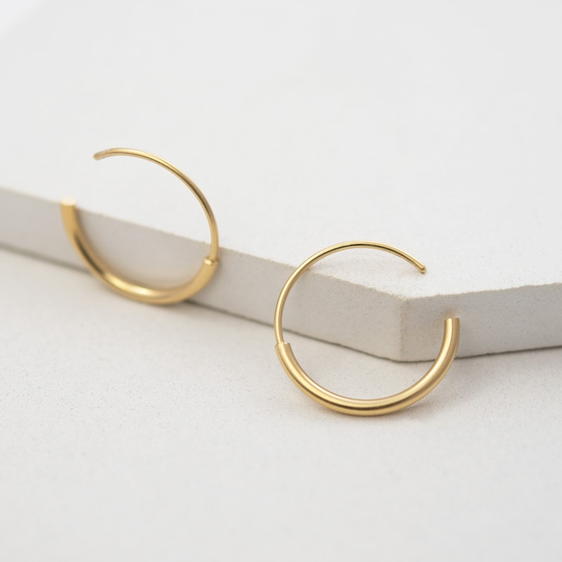 May include: A pair of gold hoop earrings. The earrings are simple and elegant, with a smooth, polished finish.