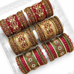 May include: Six sets of ornate bangles in a clear tray. The bangles feature intricate floral designs with red, gold, and white accents. Some sets are red, gold, and white, while others are green and red.
