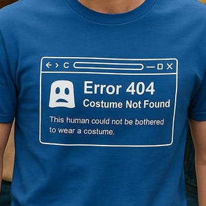 May include: A blue t-shirt with the text "Error 404 Costume Not Found" in a white box. The shirt is being worn by a person smiling, with other people in the background. The text below the error message reads: "This human could not be bothered to wear a costume."