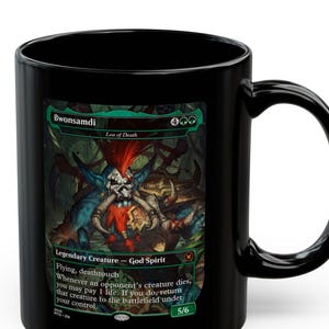 Könnte beinhalten: Schwarze Keramiktasse mit einer farbenfrohen Illustration einer Kreatur und dem Text "Bwonsamdi, Loa of Death". Die Tasse enthält auch den Text "Legendary Creature - God Spirit" und andere Spieldetails. Die Tasse hat einen gebogenen Griff.
