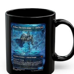 Może przedstawiać: Czarny ceramiczny kubek z fantastycznym projektem graficznym Arthasa, Króla Lisza, i tekstem. Kubek ma czarny uchwyt i błyszczące wykończenie. Projekt ma niebieską i białą kolorystykę.