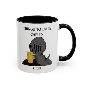 May include: White ceramic mug with a black interior and handle. The mug features a graphic of a knight in armor holding a cup, with the text "THINGS TO DO IN CAELID" and "1. DIE".