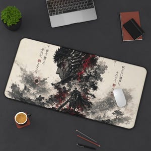 May include: A rectangular mouse mat with a black and white illustration of a warrior and Japanese text. The artwork includes a profile of a man's face, a figure with a sword, and a landscape with a flag. The mouse mat is on a dark surface.