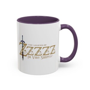 May include: White ceramic mug with a purple interior and handle. The mug features the text "THE LEGEND OF ZZZZZ IM VERY SLEEPY RIGHT NOW" in gold and a sword graphic.