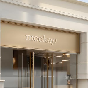 以下が含まれることがあります： 金色のファサードとガラスのドアを備えた建物の外観。 「mockup」という単語が、入り口の上に白くエレガントなフォントで表示されています。 装飾的な壁の燭台と小さな花瓶の花が見えます。