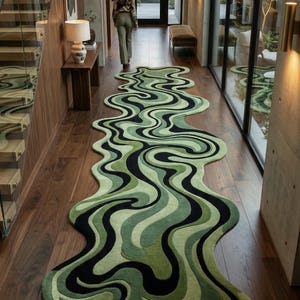 May include: A long, wavy rug with a green, black, and light green pattern. The rug is placed on a dark wood floor in a hallway. The design resembles a flowing liquid or abstract shapes.