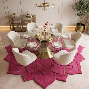 May include: A round glass dining table with a gold pedestal base, surrounded by six cream-colored upholstered chairs. The table is set with white plates, gold cutlery, and a gold tray holding candles. A large, fuchsia, petal-shaped area rug.