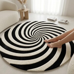 May include: A circular area rug featuring a high-contrast black and white spiral pattern that radiates from the center. The rug has a thick, textured pile surface and is laid flat on the floor, showcasing a bold, hypnotic geometric design.