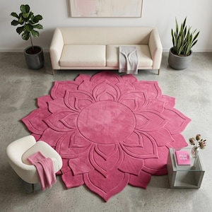 May include: A large, circular, hot pink area rug featuring a raised, carved floral petal design that radiates from a central circle. The rug has a plush, textured surface and is positioned on a gray concrete floor in a living room setting.