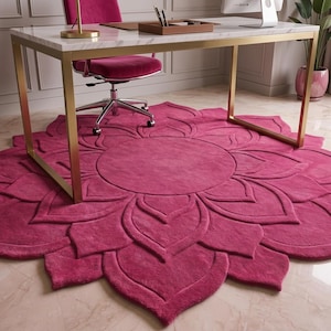May include: A large, circular, magenta-colored area rug featuring a raised, tufted floral petal pattern that radiates from a central circular core. The rug is positioned beneath a desk with a white marble top and gold-toned metal legs.