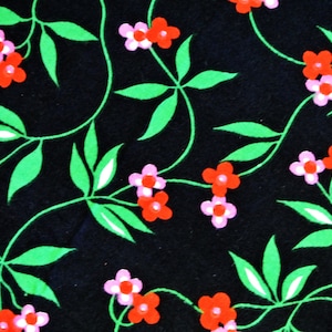 Op de afbeelding: Zwarte stof met een herhalend patroon van groene bladeren en roze en rode bloemen.