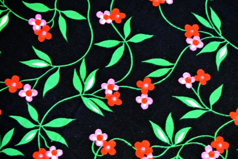Op de afbeelding: Zwarte stof met een herhalend patroon van groene bladeren en roze en rode bloemen.