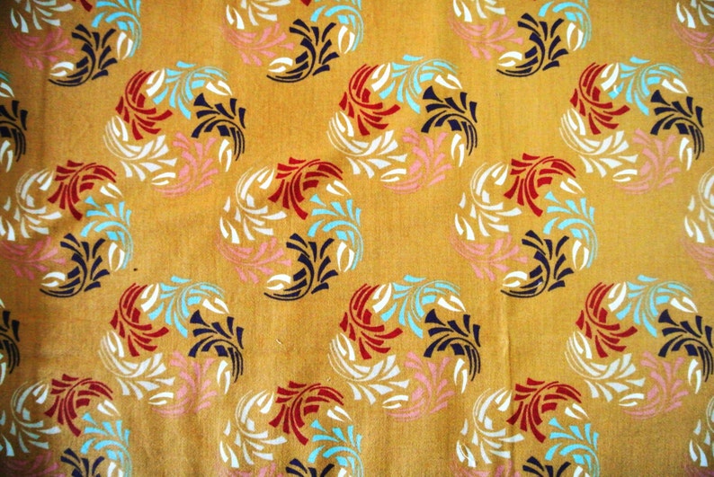 May include: A yellow fabric with a repeating pattern of stylized floral designs in white, red, blue, and pink.