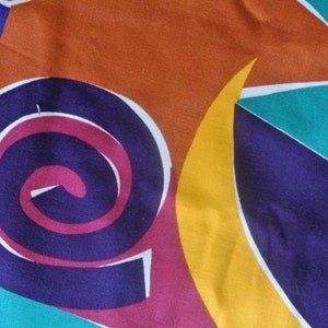 May include: Abstract fabric with a colorful geometric pattern. The pattern includes a large spiral in shades of purple, pink, and white, a yellow crescent moon, and teal and blue triangles.