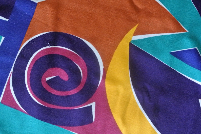 May include: Abstract fabric with a colorful geometric pattern. The pattern includes a large spiral in shades of purple, pink, and white, a yellow crescent moon, and teal and blue triangles.