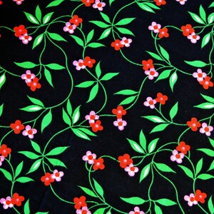 Op de afbeelding: Een zwarte stof met een herhalend patroon van roze en rode bloemen op groene ranken.