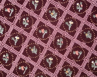 May include: A close-up of a burgundy fabric with a repeating pattern of pink squares and small floral designs in shades of pink, green, and white.
