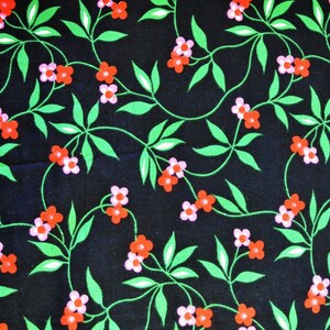 Op de afbeelding: Een zwarte stof met een herhalend patroon van roze en rode bloemen op groene wijnstokken.