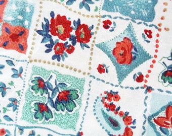 May include: A white fabric with a patchwork design featuring red, blue, and green floral patterns. The fabric has a quilted look with stitching around each square.