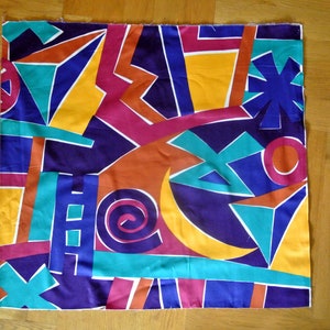 May include: A colorful fabric with a geometric pattern in shades of blue, yellow, orange, red, and green. The fabric features a variety of shapes, including triangles, squares, and circles.