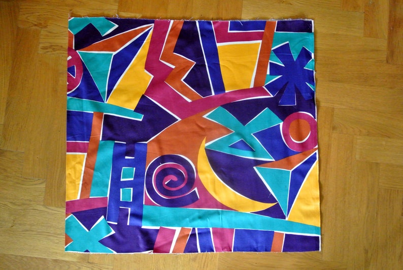 May include: A colorful fabric with a geometric pattern in shades of blue, yellow, orange, red, and green. The fabric features a variety of shapes, including triangles, squares, and circles.