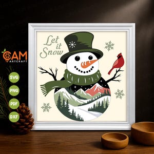 May include: A framed winter illustration featuring a snowman wearing a top hat and scarf, with a carrot nose. The snowman's body shows a snowy mountain scene. A red cardinal perches on a branch, and the text "Let it Snow" is visible.
