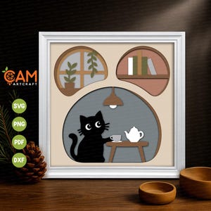 May include: A square white frame containing a layered paper art piece. The design features three arched cutouts: a window with a plant, a shelf with books, and a large central area showing a black cat sitting at a table with a teapot and cup.