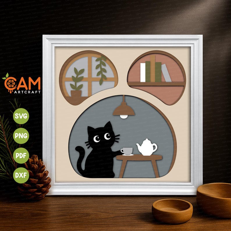 May include: A square white frame containing a layered paper art piece. The design features three arched cutouts: a window with a plant, a shelf with books, and a large central area showing a black cat sitting at a table with a teapot and cup.