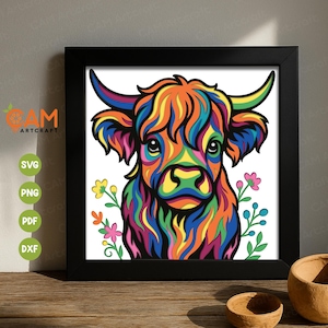 Może przedstawiać: Oprawiony wydruk przedstawiający krowę rasy Highland w żywym, tęczowym wzorze. Grafika jest oprawiona w czarną ramę i zawiera kwiatowe detale. Wydruk jest prezentowany na drewnianej powierzchni. Obraz jest kolorową reprezentacją zwierzęcia.