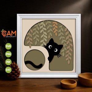 May include: A square white frame containing a layered paper art piece featuring a black cat peeking from behind a beige archway. The design includes hanging willow-like leaves in shades of green and tan, with a black cat tail visible in a circular cutout.