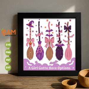 May include: A framed print featuring five decorative witch brooms in shades of brown, purple, and pink, adorned with bows, bats, and stars. The phrase "A Girl Gotta Have Options" is displayed below the brooms, perfect for Halloween decor.
