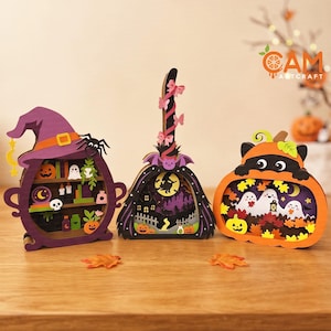 Peut inclure: Trois décorations d'Halloween en bois superposé comprenant un chaudron violet avec un chapeau de sorcière, un balai avec une silhouette de sorcière et une citrouille orange avec des fantômes. Chaque pièce présente des découpes détaillées.