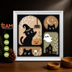 Può includere: Un'opera d'arte in carta stratificata con cornice quadrata bianca che presenta motivi di Halloween. Il design include gatti neri, un fantasma bianco, una zucca, un ragno con ragnatela, una luna crescente, stelle e una piccola bottiglia su sfondi color sabbia.